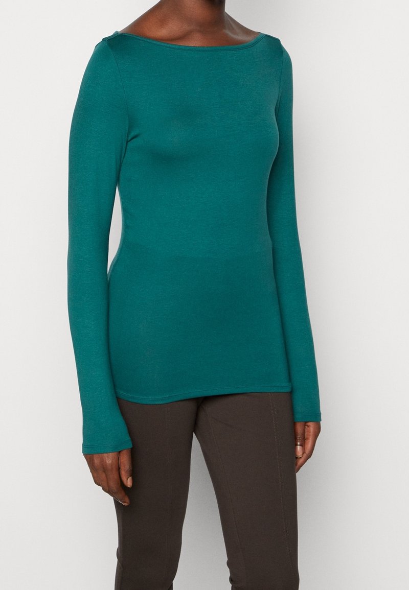 Teal långärmad topp med bred båtkrage, tillverkad av ett mjukt, lätt material. Har en figursydd silhuett och mjuk textur.