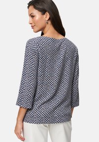 Marineblauwe blouse met een geometrisch patroon, driekwartmouwen en een ronde halslijn, gecombineerd met witte broek.