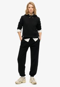 Czarna bluza z kapturem z przednią kieszenią, nałożona na białą koszulę. Połączona z czarnymi dresami i beżowymi sneakersami. Prosty design, luźny krój.