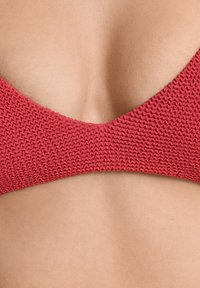 Rdeča teksturirana bikinijeva zgornja del s trikotno obliko. Pleten material z gladko zadnjo stranjo, ki se ponaša z nizkim izrezom in minimalno pokritostjo.