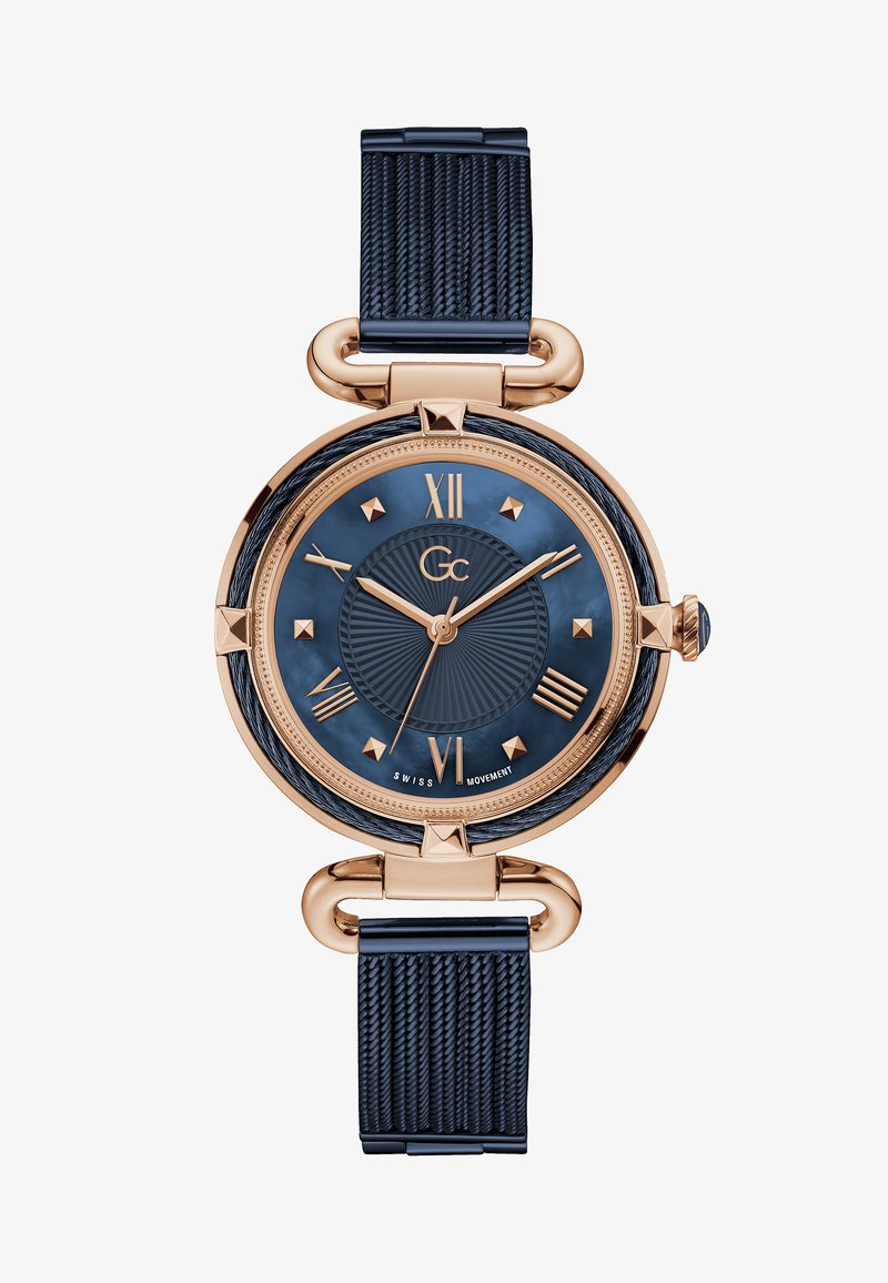 Rozā zelta pulkstenis ar tumši zilu ciparnīcu, romiešu skaitļiem un teksturētu siksniņu. Aizsargā apaļa korpuss ar studētiem akcentiem un Šveices mehānismu.