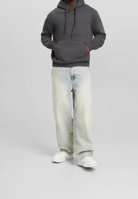 Grå huvtröja med ficka framtill, i kombination med ljusblå jeans med en urtvättad look och vita sneakers.