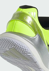 Gros plan sur le talon d'une chaussure de sport jaune néon et argentée avec une semelle blanche texturée et des détails en relief.