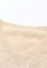 Maglione a V in morbido e chiaro beige lavorato a maglia; presenta una texture liscia e una leggera lucentezza; rifinito con bordi a costine sul colletto e sull'orlo.