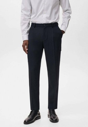 Pantalones de marinero a medida con una textura suave, pliegues frontales y bolsillos laterales. Combinados con una camisa de botones a rayas y zapatos negros.