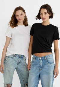 Deux modèles portant des t-shirts unis à col rond; un blanc et un noir. Tous deux associés à des jeans déchirés bleu clair. Design simple, coupe décontractée.
