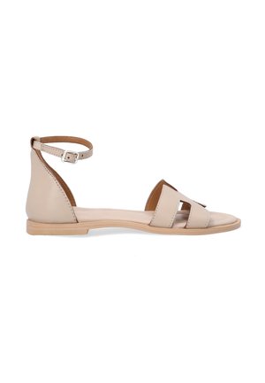 Beige leather sandal featuring a flat sole, open toe, ankle strap with buckle, and minimalist cutouts on the vamp. Smooth texture.