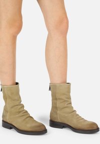 Botines de ante color beige con un diseño arrugado, punta redondeada y tacón bajo en bloque. Presentan un cierre de cremallera en la parte trasera para poner y quitar fácilmente.