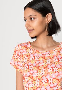 Top de manga curta em vermelho com um padrão floral apresentando flores em rosa, branco e amarelo. Decote arredondado, tecido leve, ajuste casual.