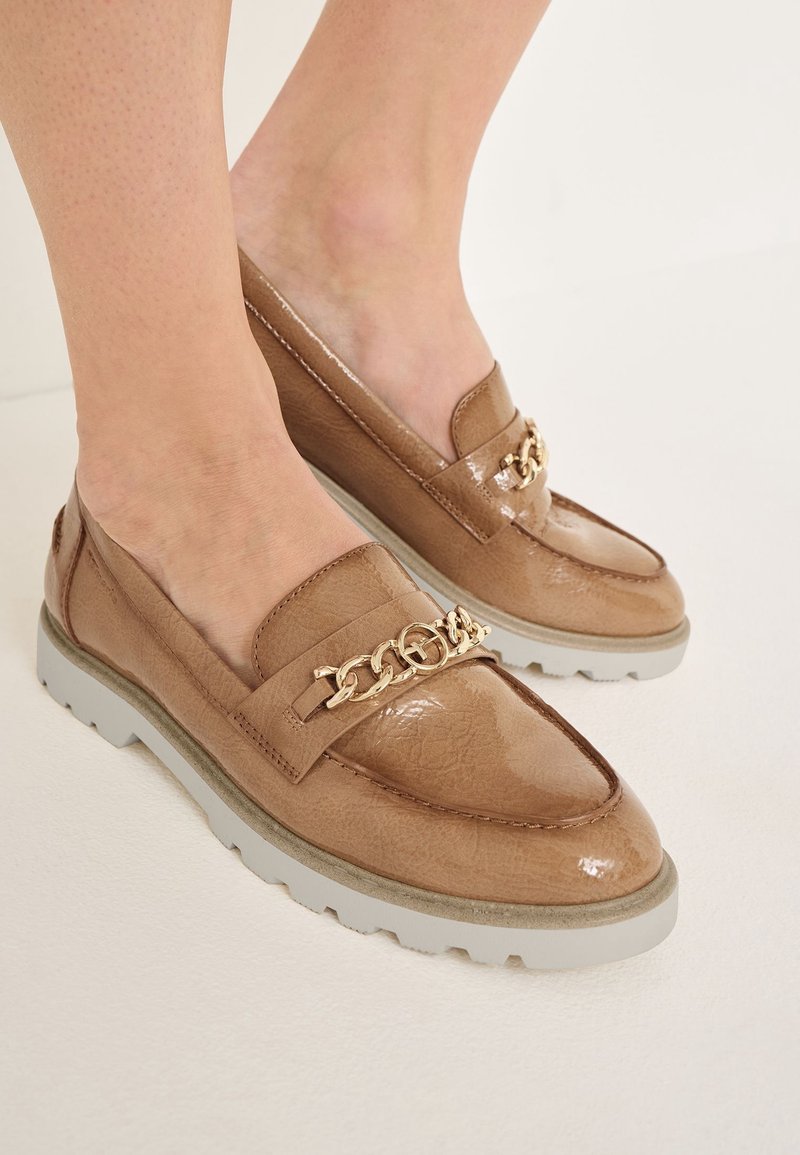 Mocassins en cuir verni marron clair avec un accent de chaîne dorée, dotés d'une semelle épaisse blanche et d'une texture lisse et brillante.