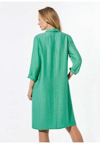 Grün, knielanges Kleid mit Kragen und hochgerollten Ärmeln. Hergestellt aus einem leichten, strukturierten Stoff. Einfaches, gerades Design.