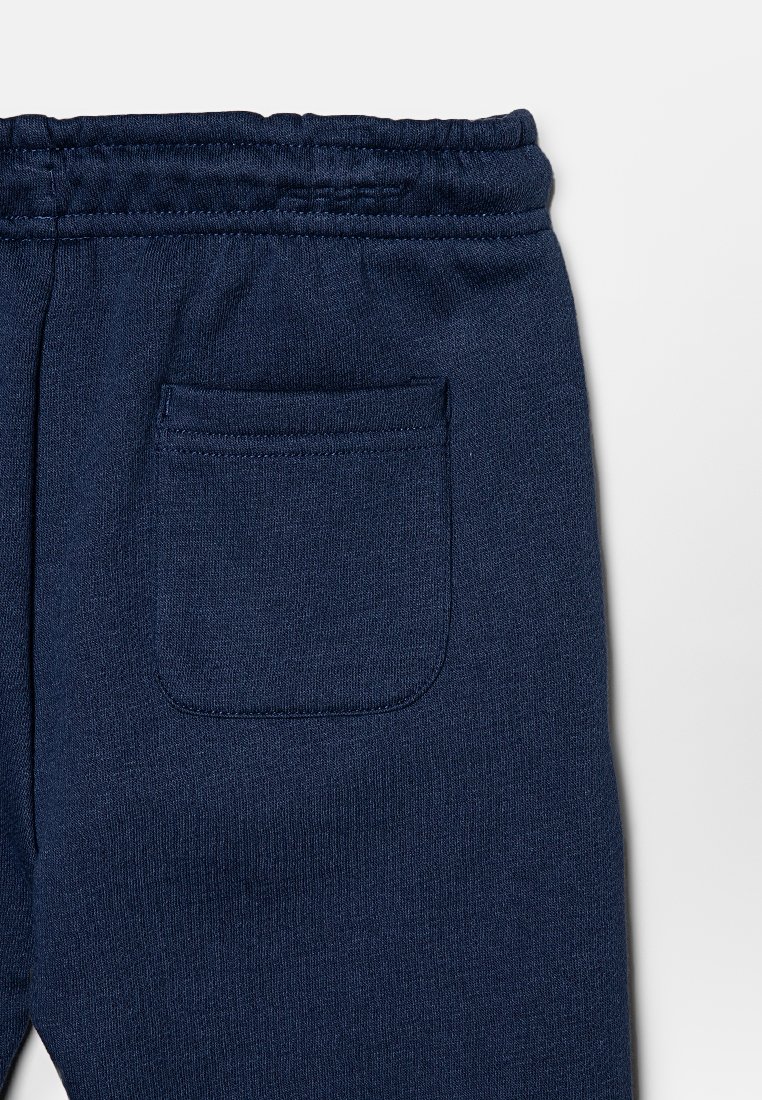 Pantalons de survêtement bleu marine avec taille élastique et une seule poche arrière, présentés sur un fond clair et uni.