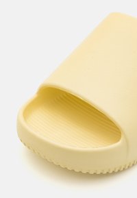 Gul skumglidesandaler med åpen tå-design, teksturert innside, glatt utside og riller på sålen for grep.