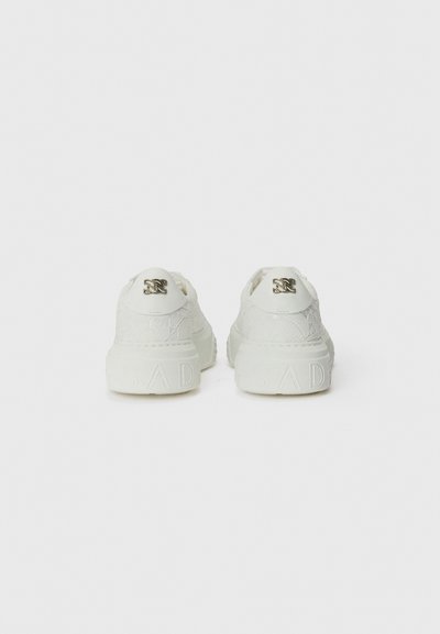 Vita sneakers med en texturerad överdel, vadderad krage och präglad branding på hälen. Designen inkluderar metalliska detaljer.