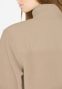 Beige fleecejakke med høj krave, kontrasterende glat panel på den øvre ryg og en tekstureret nederste sektion.