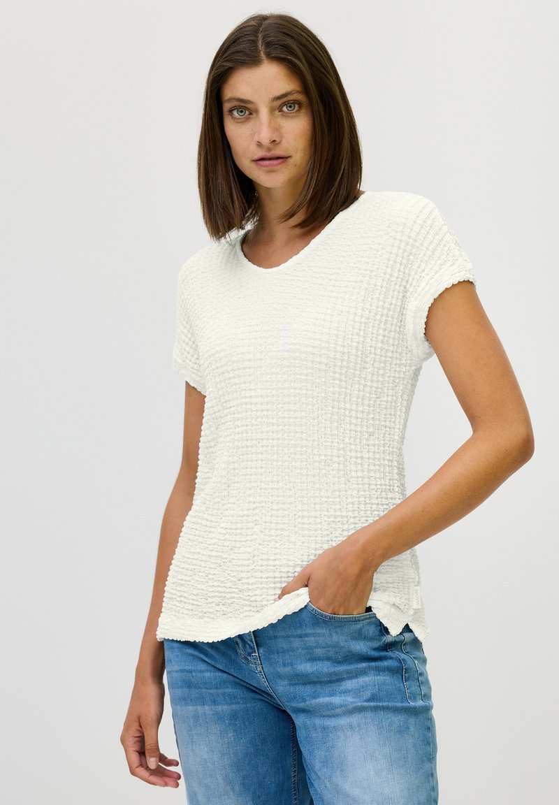 Witte gestructureerde T-shirt met korte mouwen en een ronde halslijn, met een iets ruime pasvorm, gecombineerd met lichtblauwe jeans.