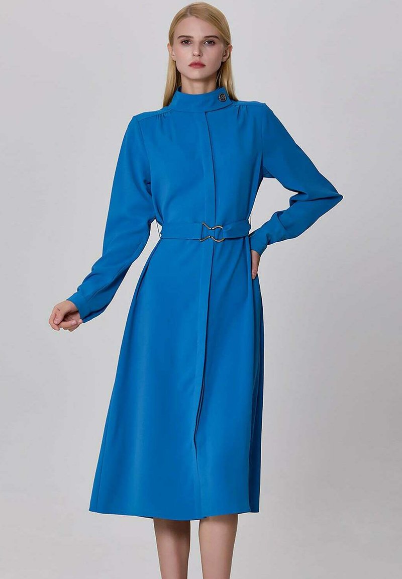 Robe bleue à manches longues avec col montant, taille ceinturée et fermoir décoratif. Texture lisse et design jusqu'aux genoux.