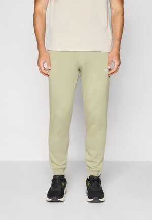Lyse olivengrønne joggebukser med smal passform, laget av mykt stoff, med en liten hvit logo på venstre lår, kombinert med svarte joggesko.