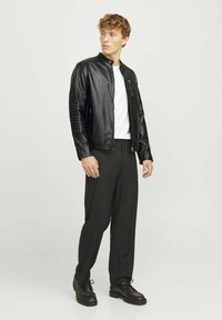 Jachetă din piele neagră cu accente ribbate la umeri, purtată peste o cămașă albă, asociată cu pantaloni negri și pantofi negri. Design simplu și modern.