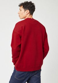 Rode sweatshirt gemaakt van zachte stof, met een ronde hals, lange mouwen en een losse fit. De achterkant toont minimale stikdetails bij de halslijn.