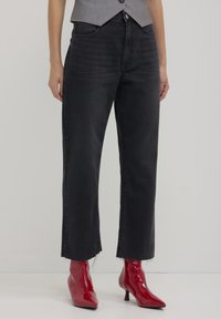 Jeans neri a gamba dritta con orli sfilacciati, abbinati a stivali alla caviglia rossi lucidi. Il tessuto ha una texture liscia e un design classico a cinque tasche.