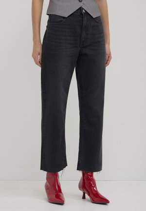 Jeans neri a gamba dritta con orli sfilacciati, abbinati a stivali alla caviglia rossi lucidi. Il tessuto ha una texture liscia e un design classico a cinque tasche.