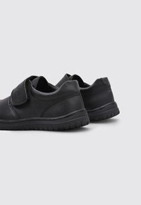 Zapatos de cuero negro con una correa de velcro, forma redondeada, suela de goma texturizada y diseño minimalista. Adecuados para uso casual.