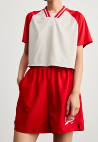 Červeno-šedý sportovní outfit značky Nike sestávající z krátkého topu s krátkými rukávy a kulatým výstřihem a červených šortek s logem.