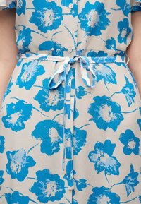 Φόρεμα ανοιχτό μπεζ με μεγάλο μπλε λουλουδένιο σχέδιο, κουμπιά μπροστά, κοντά μανίκια και υφασμάτινη ζώνη δεμένη στη μέση.