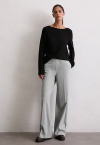 Pulover negru cu mânecă lungă asortat cu pantaloni gri cu talie înaltă și picior larg, având o textură subtilă. Încălțămintea neagră completează ținuta.