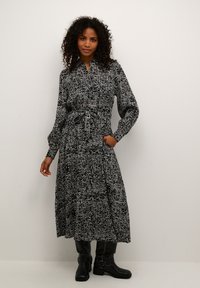 Robe midi à motif noir et blanc avec un col chemise, des manches longues, une taille nouée et une jupe fluide. Associée à des bottes noires jusqu'aux genoux.