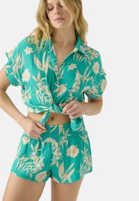 Chemise turquoise à manches courtes avec des motifs floraux, nouée à la taille, associée à un short assorti avec une taille élastique et un design similaire.