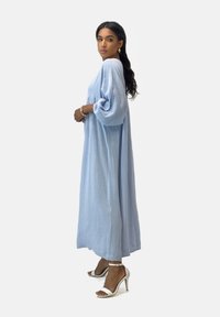 Abito maxi azzurro chiaro, con texture, maniche lunghe, una vestibilità ampia e spacchi laterali. Indossato con tacchi a spillo argentati.