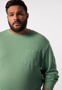 Camisa de manga larga de punto waffle verde con escote redondo y un bolsillo en el pecho, con una tela texturizada y un corte relajado.