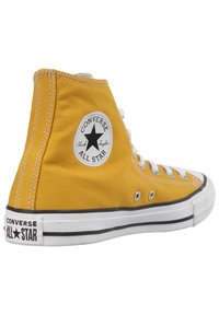 Gul duk hög topp sneakers med vita snören, gummitå, och svarta accenter. Har en cirkulär logotypapplikation på sidan.