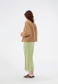 Μπεζ σουέτ τζάκετ με σχέδιο γιακά, σε συνδυασμό με ανοιχτό πράσινη φούστα με σκίσιμο και καφέ αθλητικά παπούτσια με λευκές λεπτομέρειες.