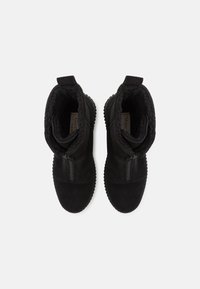 Paire de bottes d'hiver en daim noir avec doublure en laine, équipées de fermetures éclair latérales, vues de dessus sur un fond blanc.