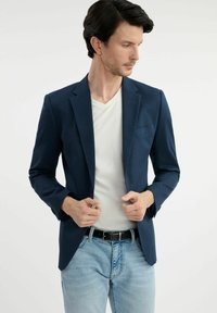 Granatowa marynarka o dopasowanym kroju i klapach, zestawiona z białym t-shirtem z dekoltem w serek oraz jasnoniebieskimi dżinsami. Gładka tekstura materiału.