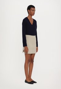 Navy genser med v-hals laget av mykt stoff, parret med et beige miniskjørt med sidelabber. Modellen har på seg svarte leiligheter.