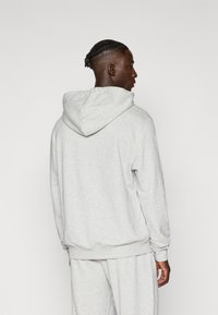 Γκρι, κουκούλα φούτερ φτιαγμένο από μαλακό υλικό. Διαθέτει πλεκτές μπαλκονάτες μανσέτες και στρίφωμα, υφασμάτινη υφή και χαλαρή εφαρμογή. Πίσω άποψη.