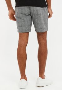 Pantalones cortos a cuadros grises hechos de tela ligera, con un ajuste entallado y un dobladillo recto, combinados con zapatillas blancas.