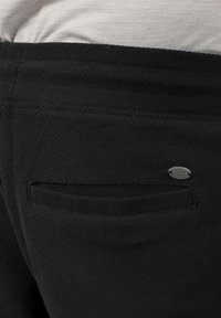 Pantalons noirs en matériau texturé avec un petit détail en métal et une poche arrière unique. Présente un motif côtelé subtil.