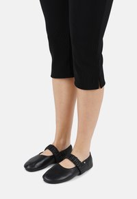 Bailarinas de cuero negro con punta redonda, tira elástica y acabado suave, combinadas con pantalones negros cortos.