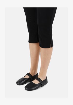 Schwarze Leder-Balletschuhe mit abgerundetem Zehenbereich, elastischem Riemen und glatter Oberfläche, kombiniert mit schwarzen, cropped Hosen.