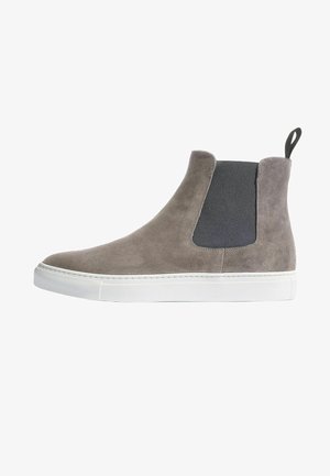 Botines de ante gris con panel lateral elástico negro, suela de goma blanca y tira en la parte posterior; acabado suave y líneas limpias.