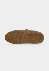 Semelle de chaussure marron avec des motifs texturés de grip en formes rectangulaires et courbes sur un fond gris clair.