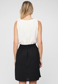 Robe noire mi-longue avec taille smockée, haut sans manches blanc avec des détails en nœud aux épaules, texture lisse et design simple.