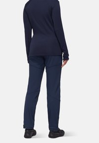 Marinblå långärmad topp i kombination med marinblå byxor med snedställda sömmar. Tyget ser mjukt ut. Svarta texturerade skor fulländar outfiten.