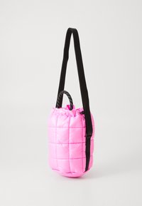 Piccola borsa a tracolla imbottita rosa con tracolla nera regolabile e manici corti in corda su sfondo bianco.
