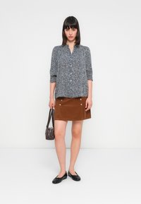 Black and white patterned blouse with button front, brown corduroy skirt with snap details, black flats, and a small brown handbag.